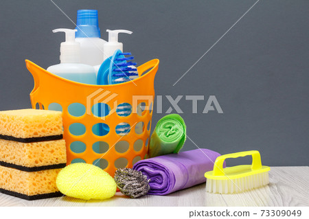 Bottles of dishwashing liquid, brush in a basket and sponges, garbage bags on gray background. Bottles of dishwashing liquid, brush in a basket and sponges, garbage bags on gray background. 73309049