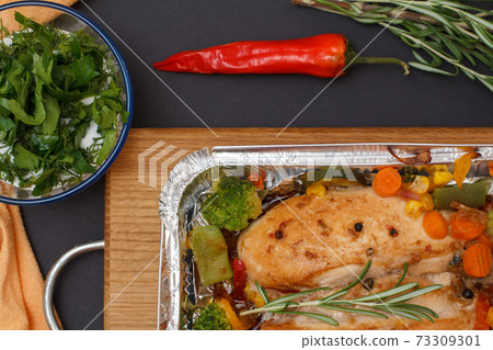 Baked chicken breasts or fillet in metal container with vegetables on cutting board. Baked chicken breasts or fillet in metal container with vegetables on cutting board. 73309301