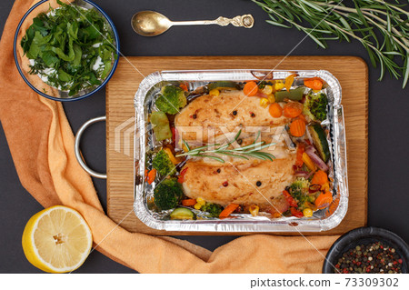 Baked chicken breasts or fillet in metal container with vegetables on cutting board. Baked chicken breasts or fillet in metal container with vegetables on cutting board. 73309302