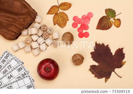 Wooden lotto barrels with bag, game cards, walnuts and apple on beige background. Autumn theme. Wooden lotto barrels with bag, game cards, walnuts and apple on beige background. Autumn theme. 73309519