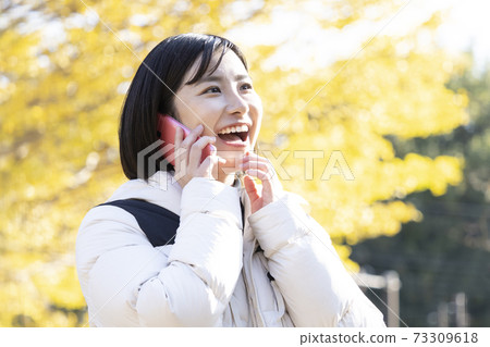 Woman calling with a smile in the autumn park Woman calling with a smile in the autumn park 73309618