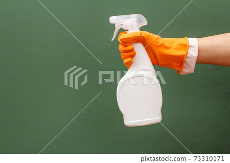 Woman's hand in protective glove with bottle of glass and tile cleaner on the green background. Woman's hand in protective glove with bottle of glass and tile cleaner on the green background. 73310171
