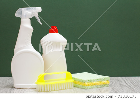 Bottles of dishwashing liquid, brush and sponges on the green background. 73310173