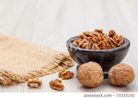 Walnuts in stone bowl with sackcloth on a wooden background. 73310192