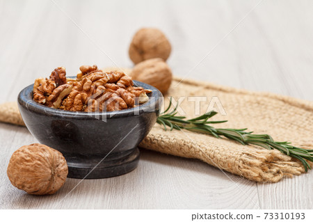 Walnuts in stone bowl with rosemary on a wooden boards. Walnuts in stone bowl with rosemary on a wooden boards. 73310193
