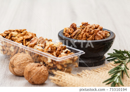 Walnuts in stone bowl and plastic container on a wooden background. Walnuts in stone bowl and plastic container on a wooden background. 73310194