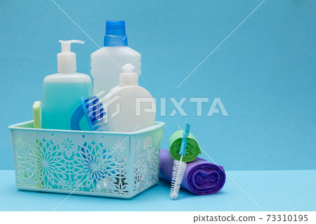 Bottles of dishwashing liquid in basket, sponges and brushes on blue background. Bottles of dishwashing liquid in basket, sponges and brushes on blue background. 73310195