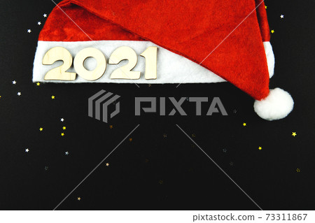 Wooden numbers 2021 on a red Santa hat on a black background. 73311867
