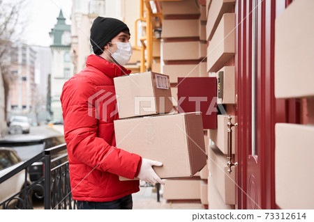Delivery guy in protective mask, handing box on doorway Delivery guy in protective mask, handing box on doorway 73312614
