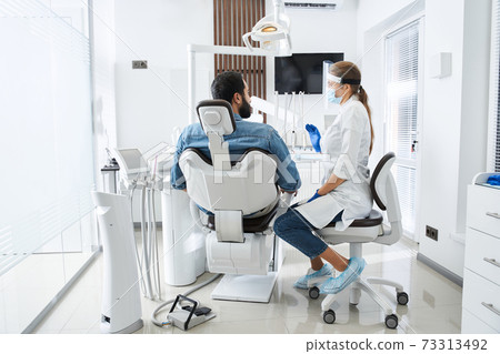 Dentist talking with patient and preparing for the treatment Dentist talking with patient and preparing for the treatment 73313492