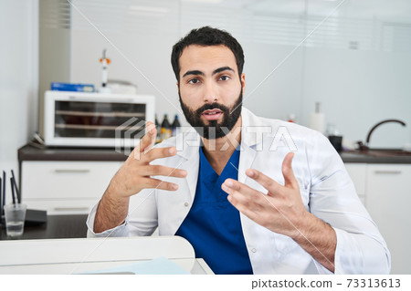 Male dentist communicating with his patient via internet connection Male dentist communicating with his patient via internet connection 73313613