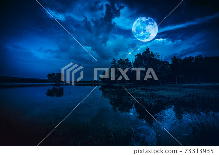 Beautiful full moon and cloudy on blue sky above silhouettes of trees, lake area. Beautiful full moon and cloudy on blue sky above silhouettes of trees, lake area. 73313935