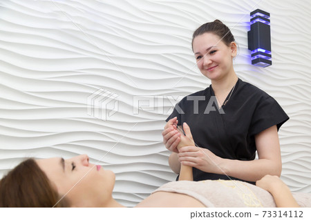 Masseur in black robe doing hand massage to a lying client Masseur in black robe doing hand massage to a lying client 73314112