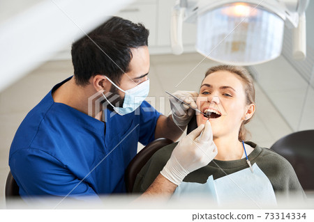 Blond-haired lady having her teeth examined by serious doctor 73314334