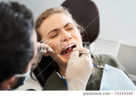 Blond-haired lady having her teeth examined by serious doctor 73314340