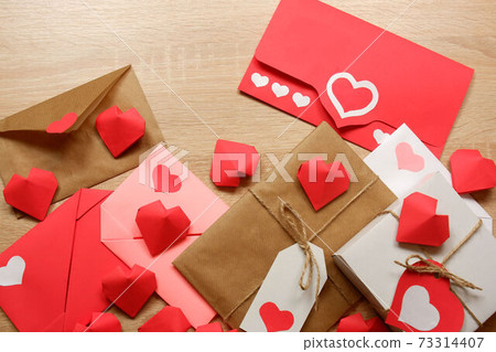 Envelopes from red paper, craft paper with hearts, red, pink, white paper envelopes, white gift box with red label in a heart form, gift wrapped in brown craft paper, tied with twine with a bow Envelopes from red paper, craft paper with hearts, red, pink, white paper envelopes, white gift box with red label in a heart form, gift wrapped in brown craft paper, tied with twine with a bow 73314407