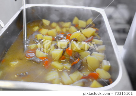 Potatoes with meat and vegetables are cooked in a large saucepan. Cooking food in the public dining Potatoes with meat and vegetables are cooked in a large saucepan. Cooking food in the public dining 73315101