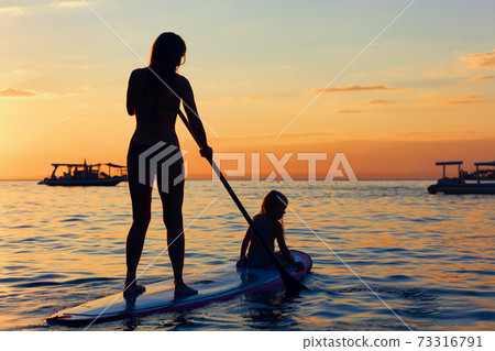 Young mother with little clild paddling on stand up paddleboard 73316791