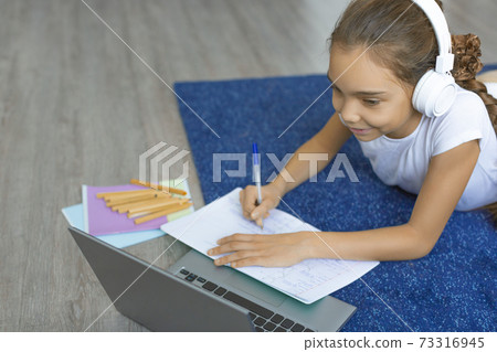 Top view of a pupil girl doing homework on the floor at home in front of a laptop monitor. Top view of a pupil girl doing homework on the floor at home in front of a laptop monitor. 73316945