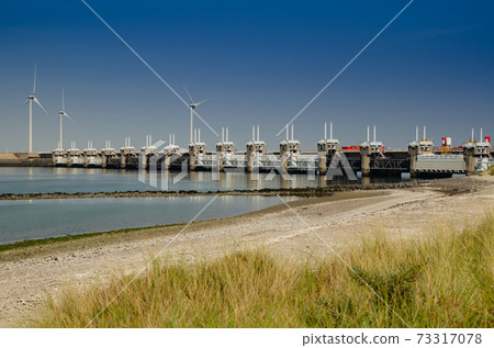 Netherlands, August 2019. In Zeeland, wind farms are the setting for the immense dam that governs the flow of sea waters, securing the territory. Netherlands, August 2019. In Zeeland, wind farms are the setting for the immense dam that governs the flow of sea waters, securing the territory. 73317078
