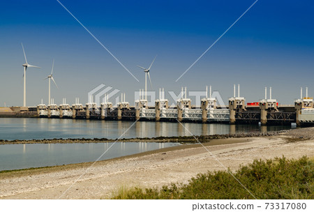 Netherlands, August 2019. In Zeeland, wind farms are the setting for the immense dam that governs the flow of sea waters, securing the territory. 73317080