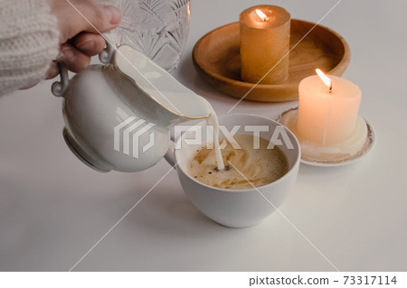 Feminine hand pouring milk from vintage style milk jug into cup of coffee Feminine hand pouring milk from vintage style milk jug into cup of coffee 73317114