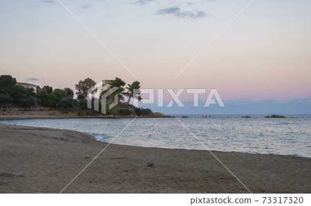 view of empty Spiaggia di Santa Maria Navarrese sand beach with green trees and old stone tower Torre Saracena in village Santa Maria Navarrese, Sardinia, Italy. Golden hour light 73317320