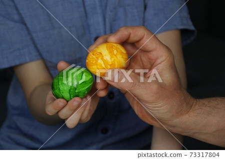 the child holds one green egg in his hand, the adult has yellow, the concept of Easter fun the child holds one green egg in his hand, the adult has yellow, the concept of Easter fun 73317804