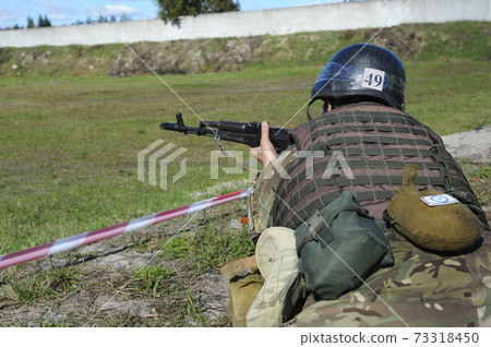 On a military shooting range: fully equipped soldier aiming at cockshies with Kalashnikov machine gun 73318450