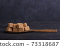 Cubes of cane sugar in a wooden spoon on a dark background 73318687