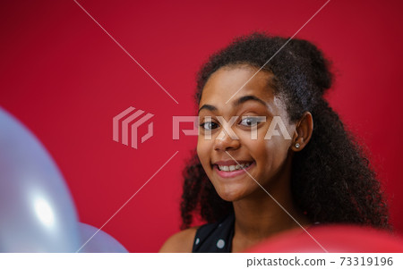 Young teenager girl in a studio on red background, looking at camera. Young teenager girl in a studio on red background, looking at camera. 73319196