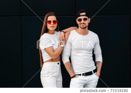A beautiful couple in love in white stylish clothes are walking in the city A beautiful couple in love in white stylish clothes are walking in the city 73319280