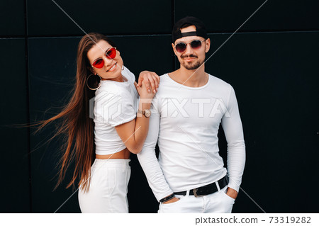 A beautiful couple in love in white stylish clothes are walking in the city A beautiful couple in love in white stylish clothes are walking in the city 73319282
