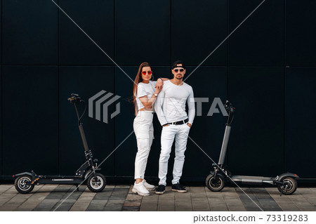 A girl and a guy are walking on electric scooters around the city, a couple in love on scooters. A girl and a guy are walking on electric scooters around the city, a couple in love on scooters. 73319283
