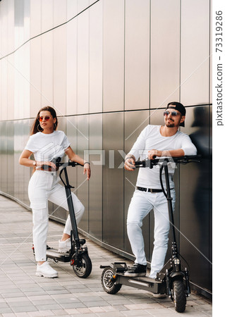 A girl and a guy are walking on electric scooters around the city, a couple in love on scooters. A girl and a guy are walking on electric scooters around the city, a couple in love on scooters. 73319286