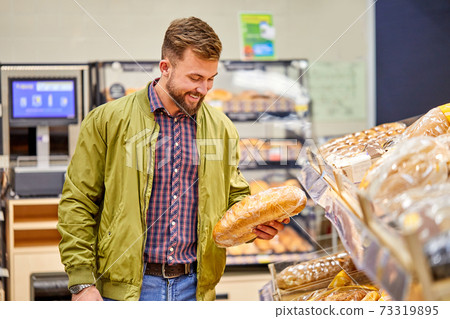 man chooses a fresh bread loaf in the supermarket 73319895