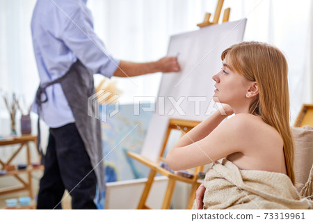 painter at the easel draws female model sitting on sofa painter at the easel draws female model sitting on sofa 73319961