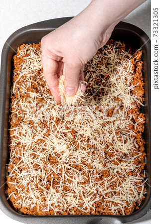 Sprinkle the grated cheese on a layer of minced meat with tomato paste. Sprinkle the grated cheese on a layer of minced meat with tomato paste. 73321305