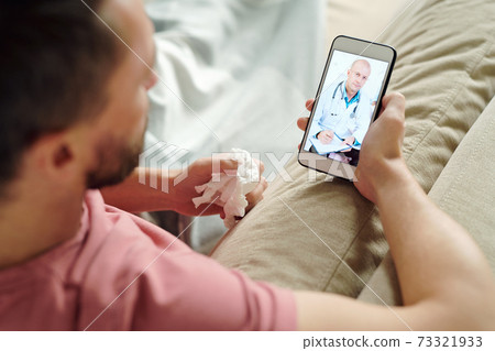 Confident doctor giving medical recommendations to young sick man lying on couch Confident doctor giving medical recommendations to young sick man lying on couch 73321933