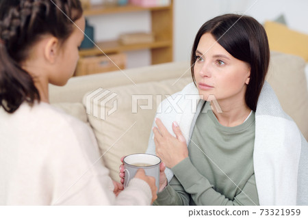 Young brunette sick female wrapped into warm plaid looking at her daughter 73321959