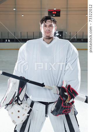 Young serious hockey player in sports uniform and gloves holding stick 73322012