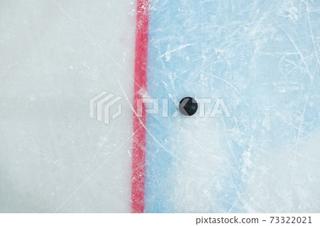 Black puck lying by red line on ice rink for playing hockey on large stadium Black puck lying by red line on ice rink for playing hockey on large stadium 73322021
