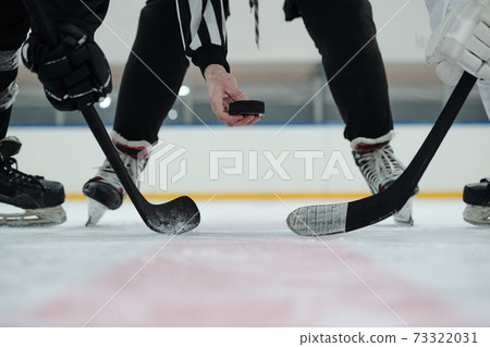 Hand of referee holding puck over ice rink with two players standing around him Hand of referee holding puck over ice rink with two players standing around him 73322031