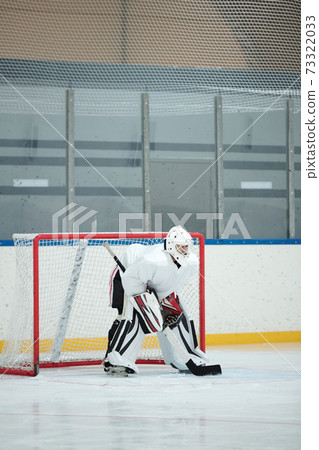 Hockey player in white sports uniform, helmet, gloves and skates holding stick 73322033