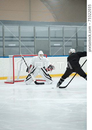 Hockey player in white sports uniform going to shoot puck during play with rival 73322035