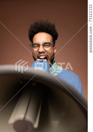 Young furious mixed-race businessman or boss in eyeglasses shouting in megaphone Young furious mixed-race businessman or boss in eyeglasses shouting in megaphone 73322152