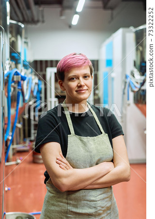 Young worker of beer production factory standing against large machines 73322252