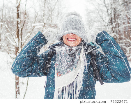 Smiling woman is playing with knitted hat. Fun in snowy winter forest. Woman laughs as she walks through wood. Sincere emotions. 73322471