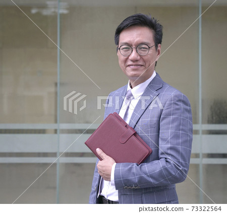 Portrait of a smiling businessman in jacket and holding a diary. 73322564