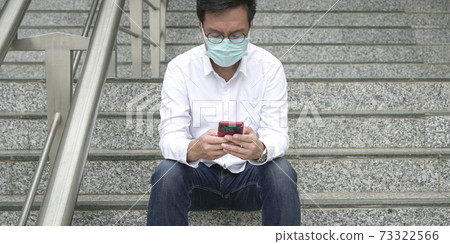 Businessman wearing face mask sitting on staircase, using and reading his phone. 73322566